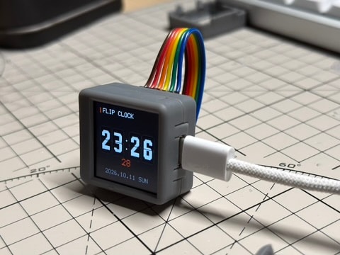 灰色 ESP32-C6 小屏摆在切割垫上，背后插着拱起的彩色杜邦线，右侧连接 USB-C 线，屏幕显示时钟